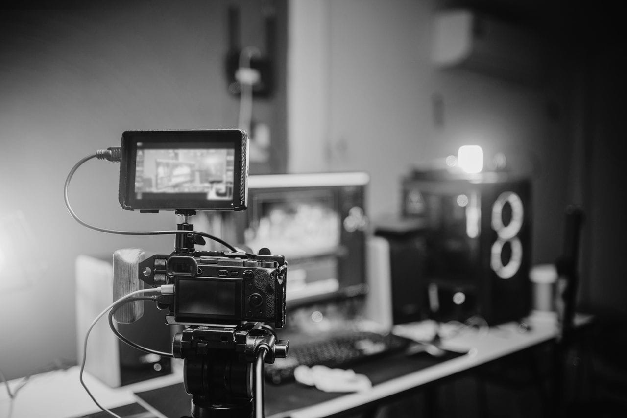 Caméra montée sur trépied dans le studio BGM Com, écrans de montage en arrière-plan